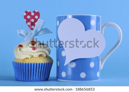 Fancy blue theme cupcake with red and white decorations with heart topper and polka dot coffee mug for birthday or special occasion gift on pale blue background.
