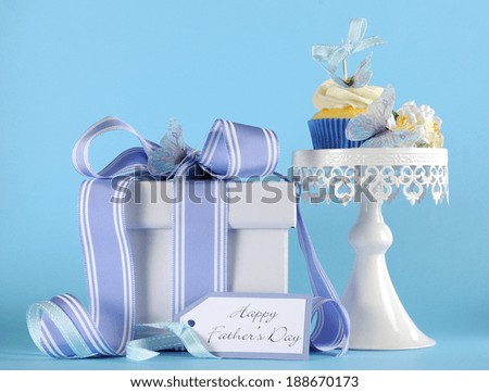 Happy Fathers Day blue butterfly theme cupcake on white cupcake stand with gift and greeting gift tag against a blue background.