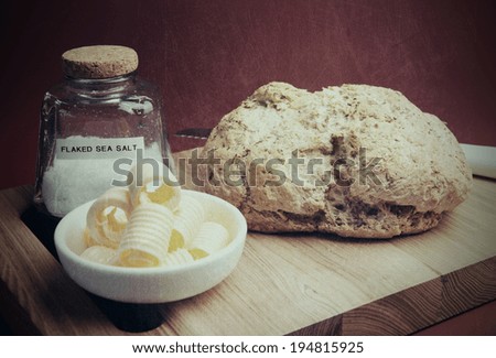 Retro vintage style homemade bread or Australian traditional beer batter damper bread with butter curls on bread board against a red brown background with Sea Salt bottle.