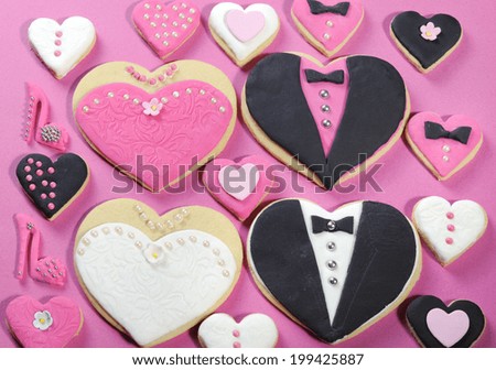 Delicious wedding party bride and groom with bridesmaid and groomsmen pink, white and black heart shape biscuit cookies bridal table favors with mini decorated hearts on a pink background.
