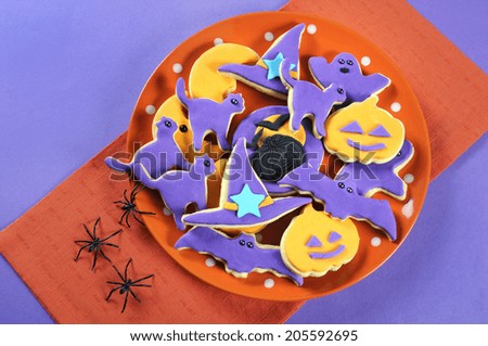 Happy Halloween orange and purple sugar cookies in cat, hat, bat and pumpkin shapes on orange and purple color blocking party table with spiders.