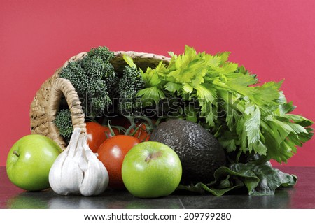 Healthy diet health foods with shopping basket full of vegetables, green apples, garlic, tomatoes, broccoli, celery and avocado against a black slate kitchen top and red wall.
