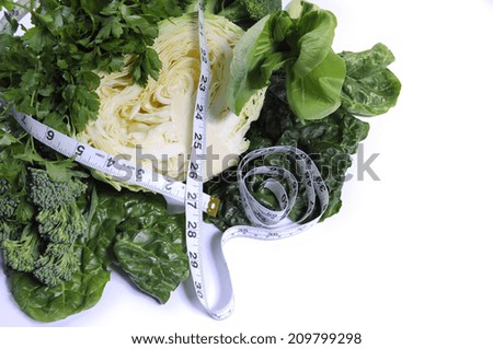 Healthy diet health foods with leafy green vegetables including cabbage, broccoli, broccolini, parsley, celery, silverbeet, and spinach with measuring tape against a white background.