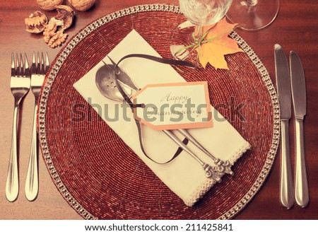 Beautiful Autumn Fall theme Thanksgiving dinner table place setting with Happy Thanksgiving tag attached to silverware. Retro vintage filter style. Aerial view with walnuts.