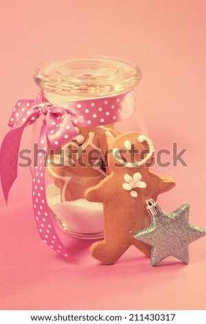 Merry Christmas festive gingerbread men in glass cookie jar with sugar against a pretty pink background with retro vintage filter.