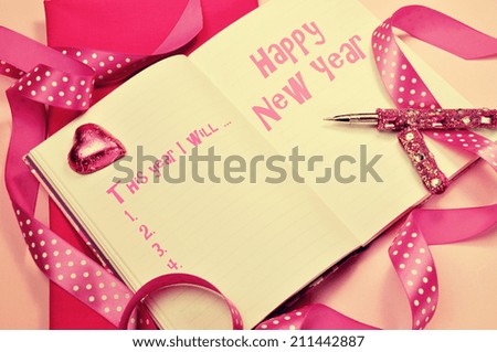 Happy New Year resolutions in diary journal book with pretty feminine pink ribbons, heart chocolate and pen with retro vintage filter.