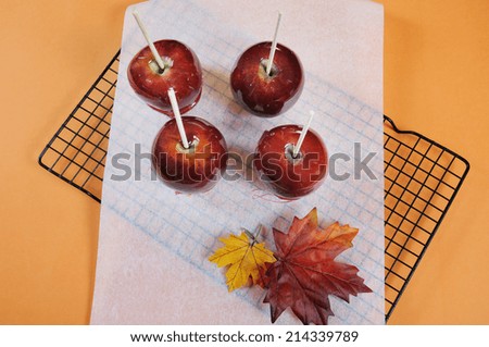 Making red toffee apples for Halloween trick or treat food candy, on baking paper and baking rack with autumn Fall leaf against an orange background - aerial.