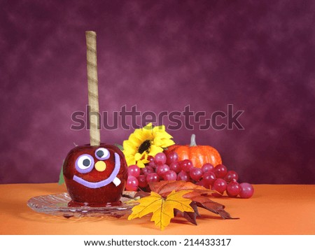 Happy smiling crazy face red toffee apple candy for trick or treat Halloween food against a bright dark pink red and orange background.