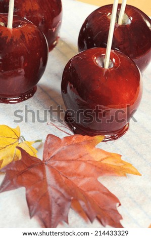 Making red toffee apples for Halloween trick or treat food candy, on baking paper and baking rack with autumn Fall leaf against an orange background - vertical close up.
