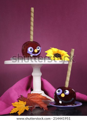 Happy smiling crazy face red toffee apples candy on stand for trick or treat Halloween food against a bright dark pink red and orange background, vertical.