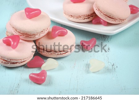 Pink macarons with pink and white jelly candy hearts on vintage blue table - close up.