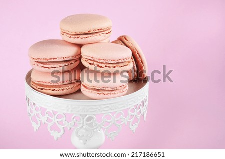 Pink macarons on white vintage style cake stand against pale pink background.