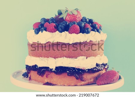 Sponge Layer Cake with fresh whipped cream, raspberry jelly and raspberries, strawberries and blueberries with retro vintage style filter.