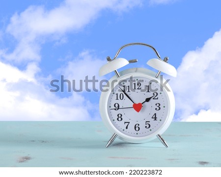 Daylight savings time white clock on a vintage aqua blue wood table against a sky with clouds background.
