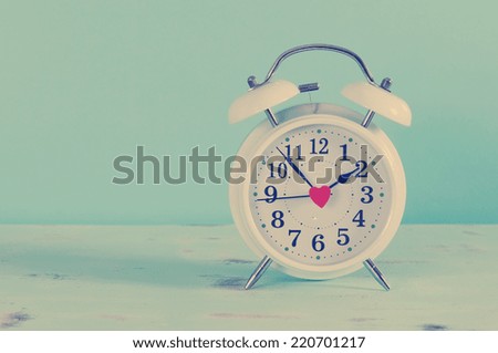 Retro vintage style classic white alarm clock on vintage blue background for daylight saving or time concept.