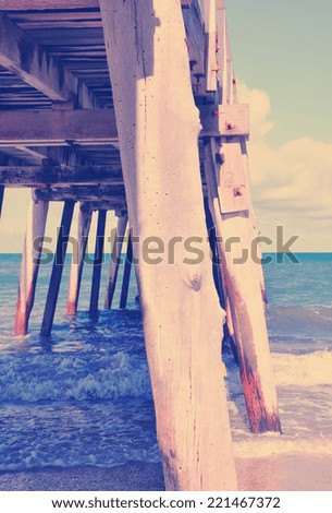 Side view of long jetty pier overlooking sandy beach with retro vintage filter. Vertical.