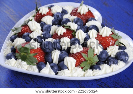 Patriotic red, white and blue berries with fresh whipped cream stars in white heart shape flag on rustic dark blue wood background. Close up.