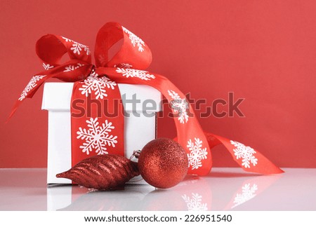 Festive red and white theme Christmas gift box on reflective white table against a red background.