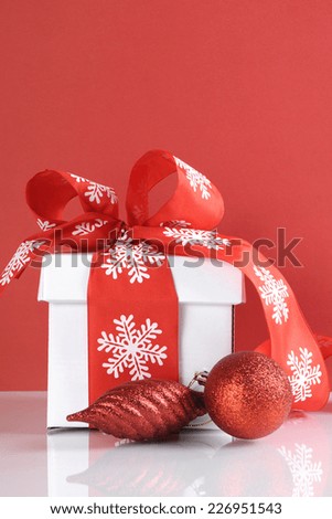 Festive red and white theme Christmas gift box on reflective white table against a red background. Vertical with copy space.