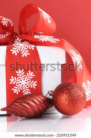 Festive red and white theme Christmas gift box on reflective white table against a red background. Close up.
