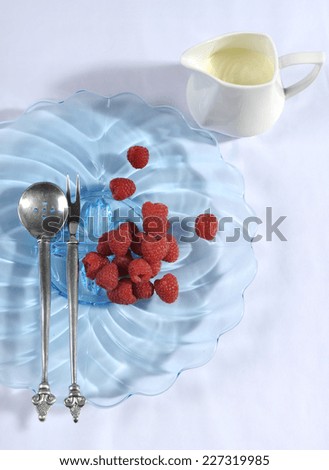 Berries and cream dessert place setting with blue vintage art deco plate and antique silverware on white tablecloth.