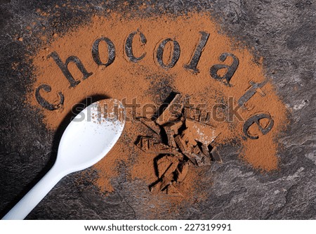 Modern aerial view of chocolate on black slate bench top table with pale blue spoon, spelling letters word with light chocolate dusting.