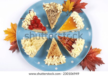 Thanksgiving apple, pecan, cherry, caramel, pumpkin spice and chocolate cream cheesecake pie, on blue polka dot platter against a white table, with autumn fall leaves.
