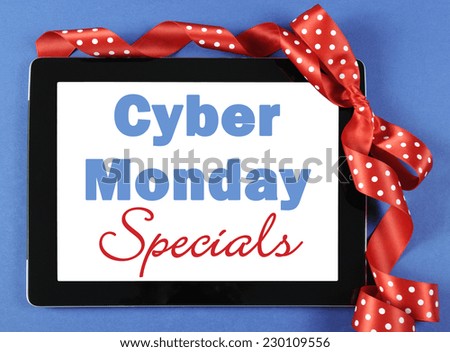 Cyber Monday Specials sale shopping sign on black computer tablet device on blue background with red polka dot ribbon.