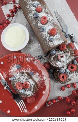 Christmas holiday chocolate roulade yule log swiss roll with berries dessert party food on red wood background. Overhead vertical.