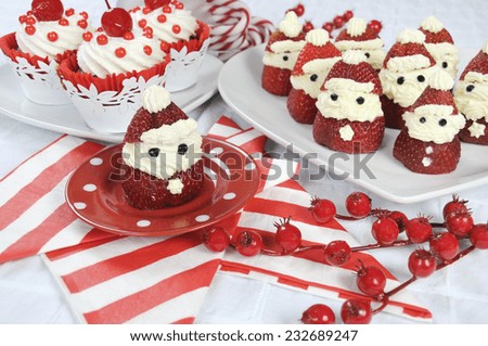 Christmas holiday Strawberry Santas with cherry red velvet cupcakes dessert party food in modern red and white theme - closeup.