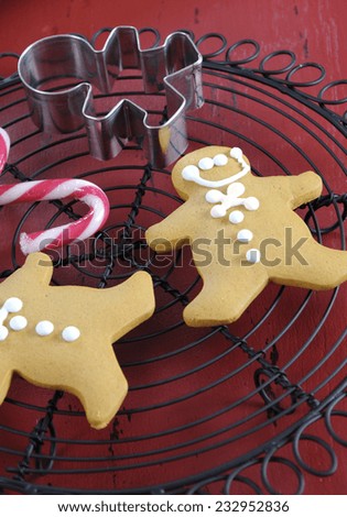 Christmas holiday festive baking with gingerbread men cookies and cookie cutter on vintage baking rack on red wood table with candy cane decorations. Vertical closeup.