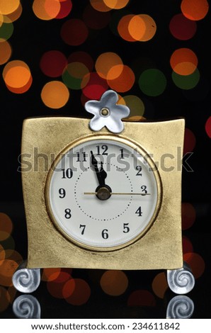 Happy New Year Eve party with gold clock and minutes to midnight time on reflective table against bright color festive bokeh lights.
