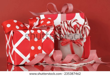 Stack of bright red and white polka dot and check festive Christmas gift boxes on red background, with stripe candy canes. Closeup.