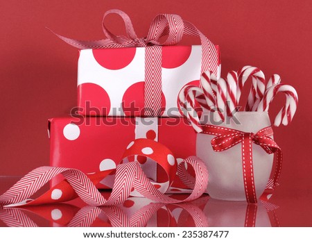 Stack of bright red and white polka dot and check festive Christmas gift boxes on red background, with stripe candy canes.