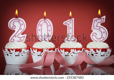 Happy New Year for 2015 red velvet cupcakes in red and white theme with lit candles on a red background,
