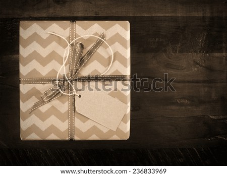 Festive gift box with chevron stripe wrapping on dark recycled wood table in sepia tones.