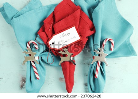 Merry Christmas table place setting red and aqua blue napkins with silver reindeer napkin holders on vintage shabby chic pale blue table.