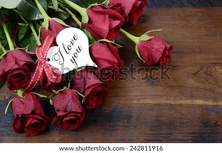 Happy Valentine\'s Day red roses on dark recycled wood background with I Love You greeting on heart shape gift tag..