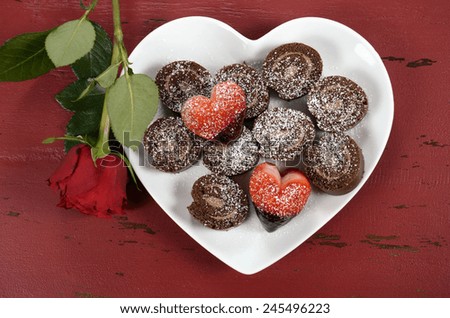Happy Valentines Day chocolate dipped heart shaped strawberries with chocolate roulade swiss roll on heart shape plate and red rose bud on red vintage wood background, overhead.