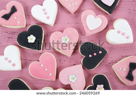 Pink, black and white homemade heart shape cookies on vintage shabby chic pink wood background for Valentines Day, wedding, Mothers Day or female birthday, overhead.