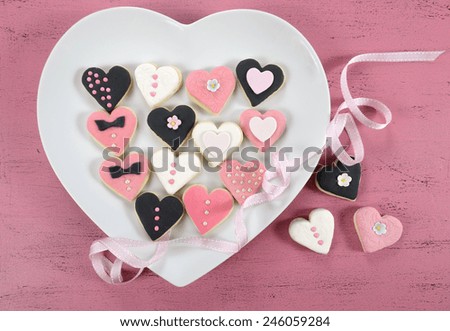 Pink, black and white homemade heart shape cookies on white heart plate on vintage shabby chic pink wood background for Valentines Day, wedding, Mothers Day or female birthday.