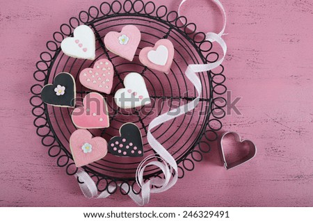 Romantic heart shape pink, white and black cookies on vintage baking rack with ribbon on shabby chic pink wood table for Valentine or wedding day.