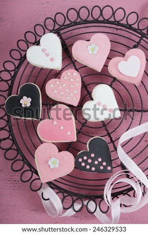 Romantic heart shape pink, white and black cookies on vintage baking rack with ribbon on shabby chic pink wood table for Valentine or wedding day, vertical.