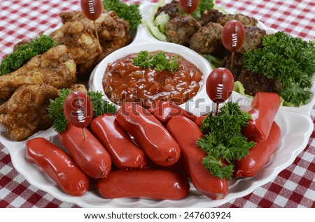 Super Bowl Sunday football party celebration food platter with chicken buffalo wings, meat balls, hot dogs and salsa dip on red check table cloth.