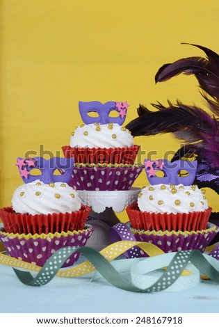 Mardi Gras cupcakes with purple mask toppers on rustic style vintage yellow and aqua blue wood background. .