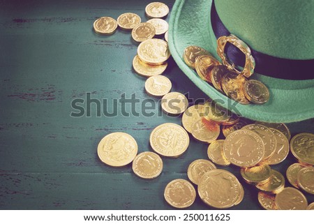 Happy St Patricks Day leprechaun hat with gold chocolate coins on vintage style green wood background, with retro vintage style filters.