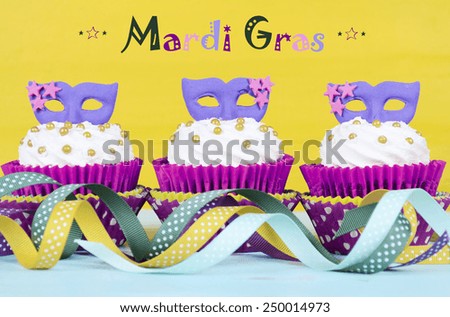 Mardi Gras cupcakes with purple mask toppers on rustic style vintage yellow and aqua blue wood bakcground, and sample text .