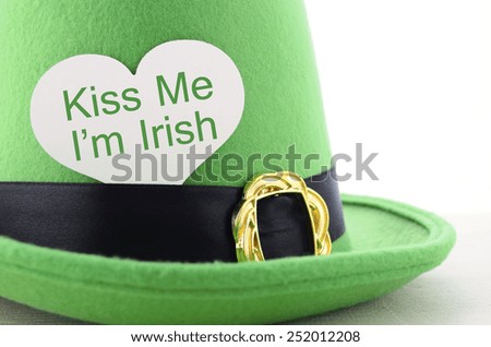 Happy St Patricks Day green leprechaun hat on white wood table with Kiss Me I am Irish heart shape greeting sign, closeup.