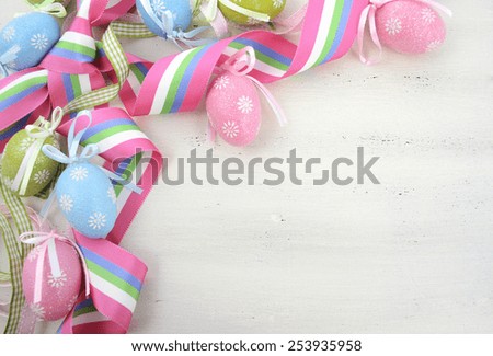 Happy Easter background with pink, blue and green ornament eggs and ribbon on vintage style rustic distressed white shabby chic wood table, with copy space for your text here.