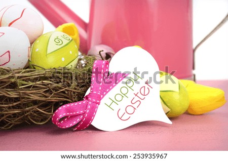 Happy Easter Spring theme pink watering can with easter eggs and eggs, nest and flowers on pink wood table against a white background, closeup with gift tag and sample tag.